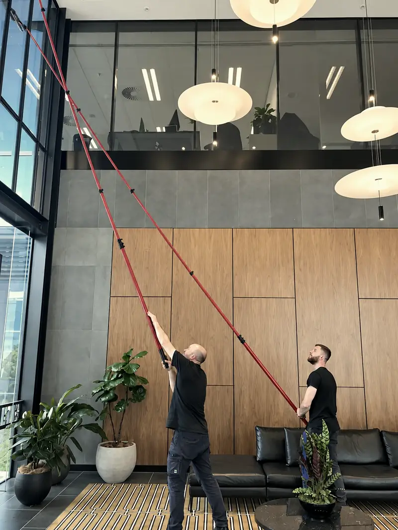 Two Tower workers using extension poles to clean high internal glazing