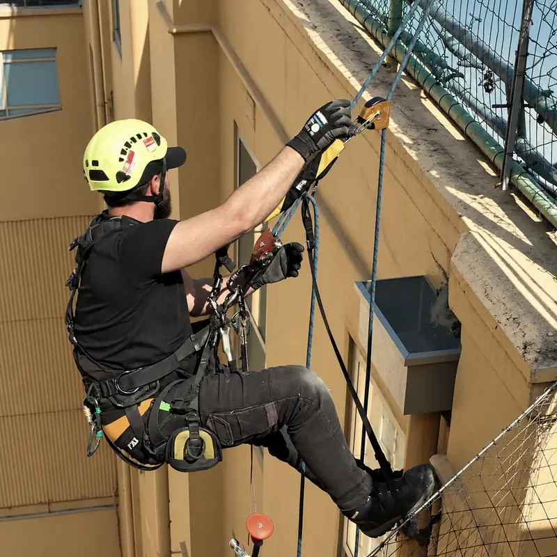 A helmeted rope-access technician operating rope equipment beside a heritage facade