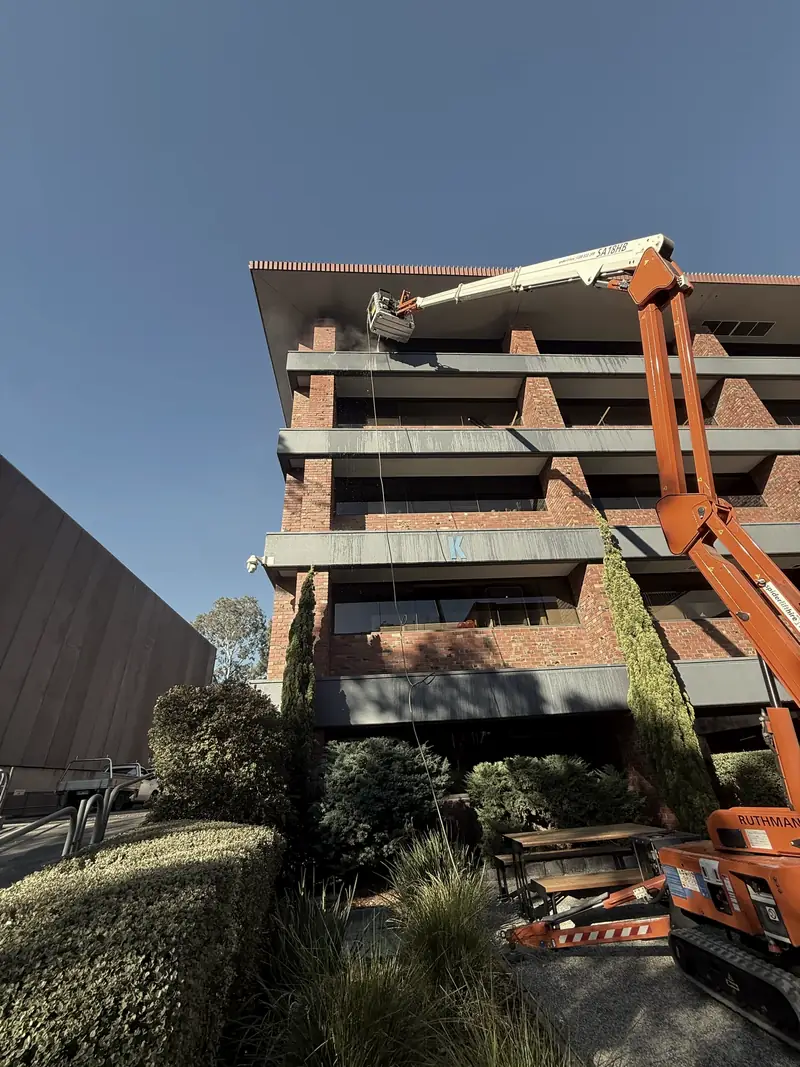 A tracked spider lift reaching the upper floors of a brick office building