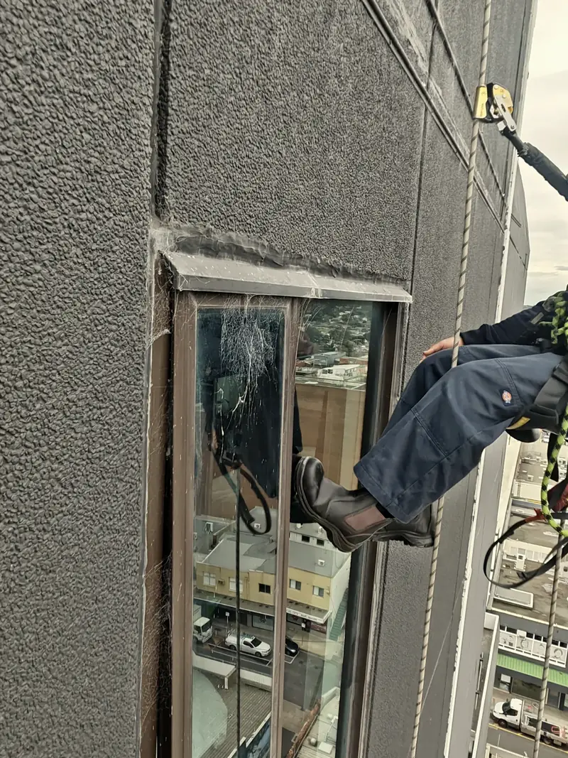 A rope-access technician working on a window seal on a concrete facade