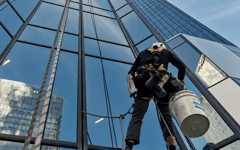 A rope-access technician on two ropes cleaning the glass of a city tower